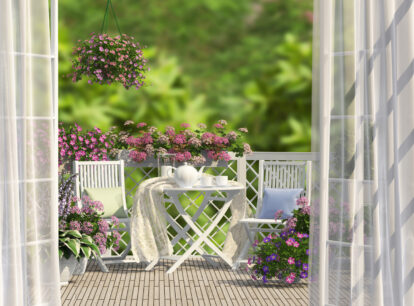 widok na balkon z białymi meblami, różowymi i fioletowymi kwiatami
